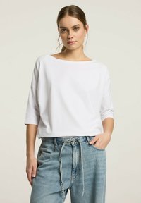 Biała, luźna bluzka z trzema ćwiartkami rękawów, wykonana z miękkiej bawełny; w zestawie z jasnodemnowymi dżinsami z wysokim stanem.