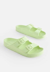 Sandales vert clair en plastique lisse, dotées de deux sangles réglables avec boucles et d'une semelle plate texturée pour une meilleure adhérence.