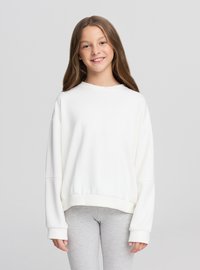 Felpa bianca con collo rotondo, spalle scese e polsini a coste, abbinata a leggins grigio chiaro su una persona in posizione neutra.