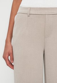 Light beige tailored pants with a smooth texture, featuring a flat front, belt loops, and side pockets. Classic straight leg design.