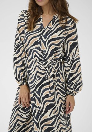 Šaty so zebrovým vzorom s dlhými rukávmi, výstrihom do V a viazaním v páse. Tkanina zobrazuje vlnité čierne, krémové a pieskové vzory.