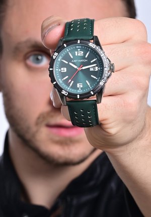 Green rubber strap watch with a black bezel, round face, white hour markers, and a red second hand. Features a date display at 3 o’clock.