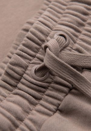 Gros plan d'une ceinture en tissu côtelé beige avec un cordon tressé passant dans des œillets métalliques.