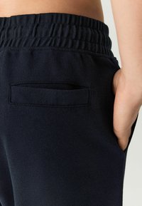 Pantalones azul marino con una tela tejida texturizada, que cuentan con una cintura elástica y un bolsillo trasero con un sutil detalle de solapa.