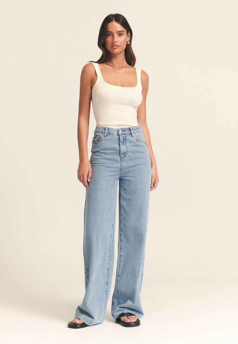 Gai bēšs ribots tanks saskaņots ar gaiši ziliem augsta vidukļa, platajiem džinsa džinsiem. Modelis nēsā melnas plakanas sandales.