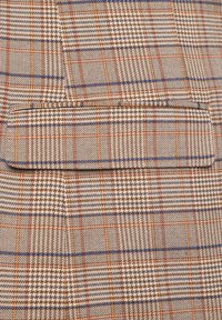 Brązowa i kremowa tkanina w kratę z niebieskimi i pomarańczowymi liniami, wyróżniająca się subtelną teksturą oraz jedną kieszenią wytyczoną wzorem.