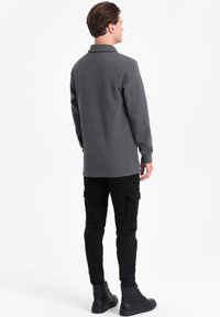 Grijze sweatshirt met een kraag, lange mouwen en zijsplitten, gecombineerd met zwarte cargobroek met meerdere zakken en zwarte laarzen.