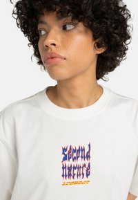 White sweatshirt featuring colorful "Second Nature" graphic, with blue and red text in a stylized font on the front. Crew neck design.