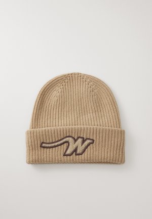 Beige gebreide beanie met een omgeslagen rand en een donkerbruin geborduurd logo dat lijkt op de letter "W." Getextureerd, geribbeld materiaal.