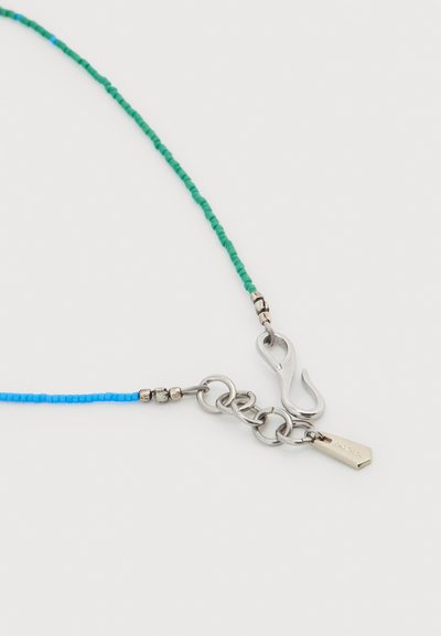 Κολιέ με μικρές μπλε και πράσινες χάντρες, ασημένιες αλυσίδες, κούμπωμα με άγκιστρο και μια μικρή ορθογώνια ασημένια ταμπέλα.