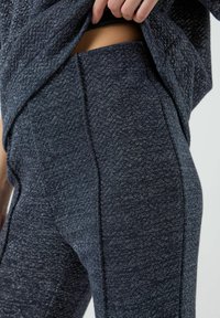 Leggings in tessuto navy testurizzato con un leggero lucido. Presentano motivi a zigzag e cuciture laterali, abbinati a un top coordinato parzialmente sollevato.