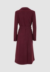 Lungo cappotto bordeaux con vita cintata, colletto a punta e maniche ampie. Tessuto liscio, design sartoriale con taglio dritto e spacco posteriore.