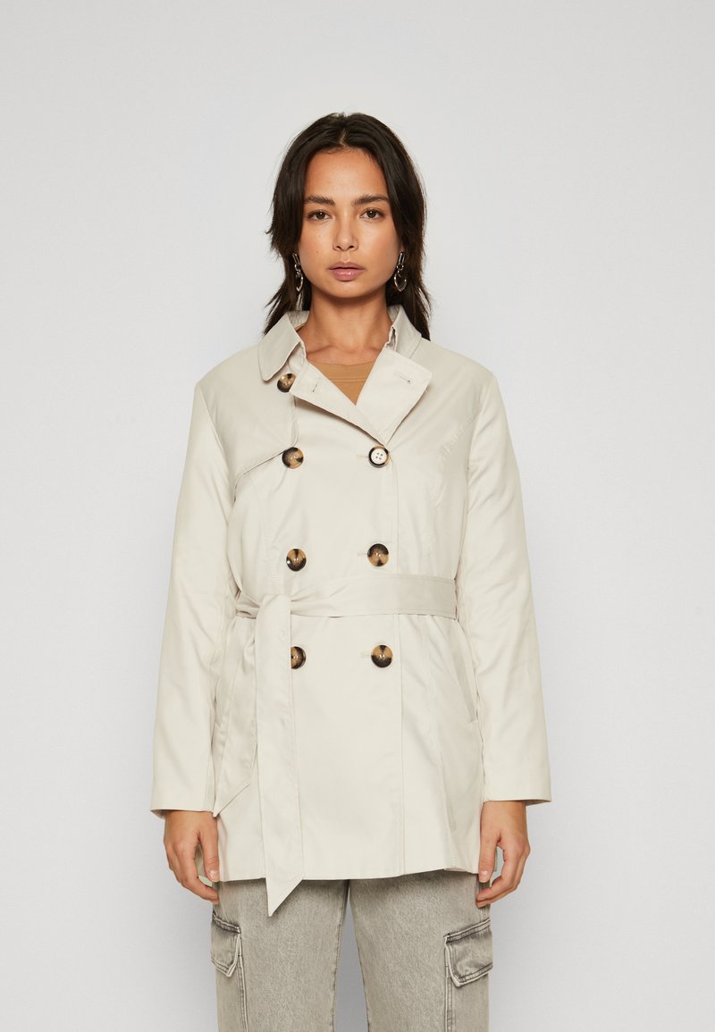 Trench coat bej deschis cu nasturi dubli, talie cu curea și guler. Textură netedă cu două buzunare laterale.