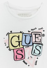 Camiseta blanca hecha de algodón orgánico. Presenta un gráfico colorido con letras en cuadrados y un texto divertido que dice "¡DIVIÉRTETE!"