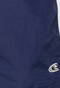 Navy blue kangas yenye uso laini, ikionyesha logo ya wimbi la rangi nyeupe iliyoembwa kwenye kona ya chini kulia.