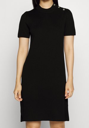 Robe courte noire à manches courtes avec un col haut, présentant une texture côtelée et trois boutons décoratifs sur l'épaule. Coupe droite.