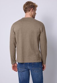 Langärmliger brauner Pullover aus strukturiertem Stoff, mit Rundhalsausschnitt und lockerer Passform, kombiniert mit blauen Jeans.