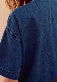 Granatowa koszula dżinsowa z krótkim rękawem, o swobodnym kroju, z widocznymi szwami i gładkim, teksturowanym wykończeniem.
