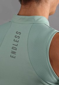 Lichtgroene mouwloze sporttop met hoge kraag, gladde textuur en "ENDLESS" verticaal op de achterkant gedrukt in zwarte lettertype.