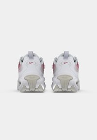 Biele športové topánky s textúrovanou podrážkou, s ružovými akcentmi na päte a šedou pútkom vzadu. Viditeľné logo Nike.