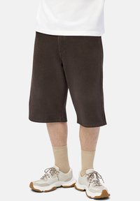 Man wearing dark brown knee-length shorts, beige ribbed socks, and white chunky sneakers with brown soles.