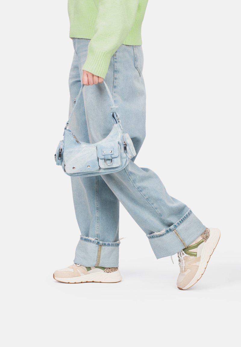 Bolso de mezclilla de color azul claro con múltiples bolsillos, herrajes plateados y una correa corta, combinado con jeans de ajuste relajado de color azul claro y zapatillas beige.