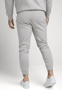 Graue Baumwoll-Jogginghosen mit gerippten Bündchen und elastischem Bund. Getragen mit weißen Sneakers mit goldenen Akzenten. Leichte Textur, körperbetonte Passform.