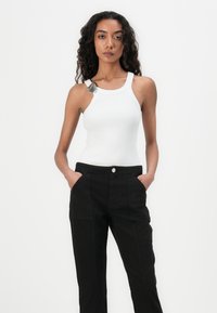 Top sin mangas blanco de canalé con diseño de espalda nadadora, que presenta una etiqueta gris. Combinado con pantalones negros de tiro alto con bolsillos frontales.