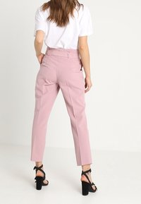 Pantalons ajustés rose clair avec une taille haute, des jambes droites et une texture lisse. Sandales noires à talons blocs avec des lanières à la cheville.