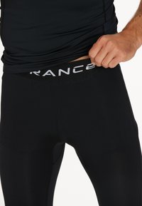 Leggings de sport noirs avec une texture lisse et une taille haute, ornés de lettres de marque blanches contrastantes à l'avant.