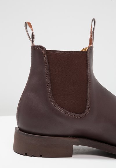 Botte Chelsea en cuir marron avec des panneaux latéraux élastiques, une languette de traction et un robuste talon en bois. Texture lisse avec des détails de couture renforcés.