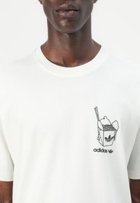 Hvit bomull T-skjorte med svart grafikk av en takeout-boks med nudler og spisepinner, samt "adidas" merkevare under designet.