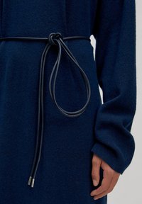 Marineblaues, langärmeliges Kleidungsstück aus strukturiertem Stoff. Es verfügt über einen abnehmbaren, geknoteten Ledergürtel mit metallischen Akzenten.