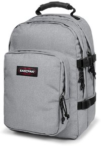 Mochila de tela gris con un gran compartimento principal, bolsillo frontal, acentos negros, correas ajustables y una asa superior. Logo de Eastpak mostrado de manera prominente.
