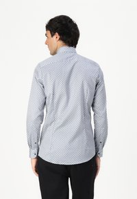 Chemise à manches longues avec un motif géométrique bleu et blanc, poignets à boutons et col montant, fabriquée à partir d'un tissu léger.