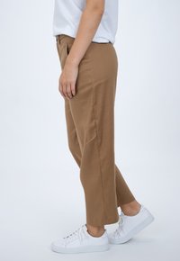 Tan trousers made of soft material with a straight cut. Paired with white sneakers featuring a smooth texture and minimal design.