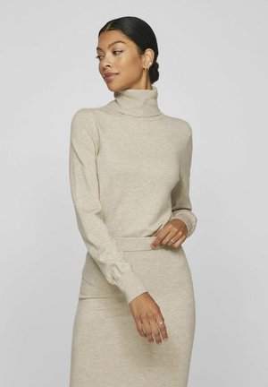 Suéter beige de cuello alto hecho de tela suave, diseño ajustado con mangas largas y puños acanalados, presentado combinado con una falda a juego.