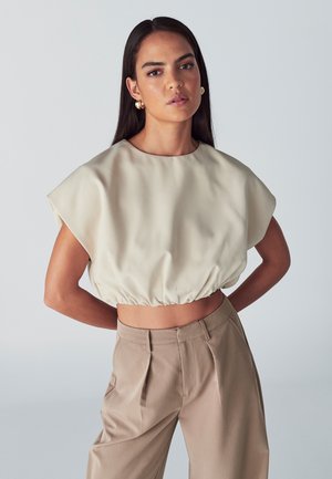 Blusa color crema a maniche larghe con orlo arricciato, abbinata a pantaloni beige a vita alta con pieghe. Texture del tessuto liscia.
