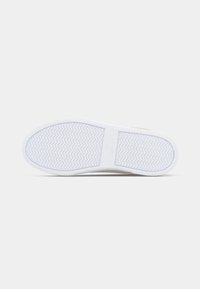 Λευκή ελαστική σόλα αθλητικού παπουτσιού με σχεδίαση πέλματος ζιγκ-ζαγκ και τη λέξη «Lacoste» στη μέση, σε απλό φόντο.