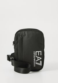 Petit sac bandoulière noir avec fermeture éclair et une sangle ajustable. Logo audacieux "EA7 EMPORIO ARMANI" affiché sur le devant.