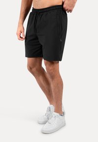 Pantalones cortos negros de tejido ligero, con cintura elástica y dos bolsillos laterales. Combinados con zapatillas altas blancas.