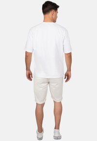 T-shirt en coton blanc avec une coupe droite et des manches courtes, associé à des shorts gris clair. Baskets avec un logo distinctif.