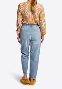 Blusa de manga larga con estampado en naranja y rosa, combinada con unos jeans de tiro alto en azul; unas suaves y texturizadas pantuflas amarillas completan el look.