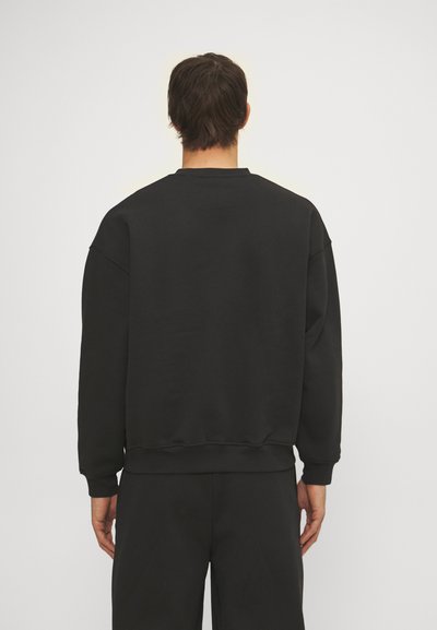 Melnā sporta krekls ar apaļu kaklu, nolaižamām plecu daļām un ribota dizaina piedurknēm un apakšmalu. Izgatavots no gludas auduma ar brīvu piegriezumu.