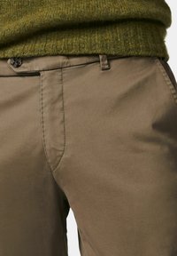 Brown cotton pants with a smooth texture, featuring a front pocket, tonal stitching, and a dark button closure at the waistband.