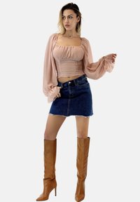 Lichtroze top met lange mouwen en gerimpeld ontwerp, gecombineerd met een denim rok. Kniehoge, bruine leren laarzen met hakken maken de outfit compleet.