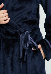 Robe bleu marine en tissu peluche doux avec un motif texturé, doté d'un lien en satin assorti et de grandes manches.