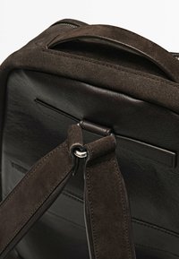 Brauner Leder- und Wildleder-Rucksack mit verstellbaren Trägern, Metallelementen und strukturiertem Oberflächendesign. Verfügt über einen oberen Griff und steppende Details.