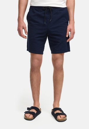 Mørkeblå teksturerede shorts med elastisk talje og snoretræk, parret med sorte sandaler med to justerbare stropper.
