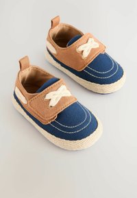 Chaussures en toile marron et bleue avec une semelle en jute tressé, présentant une sangle en croix et un épais fil blanc, conçues pour un enfilage facile.